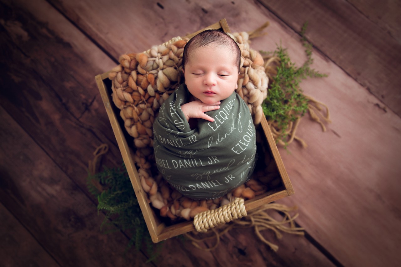 Newborn baby wrapped in a soft green blanked sitting in a box