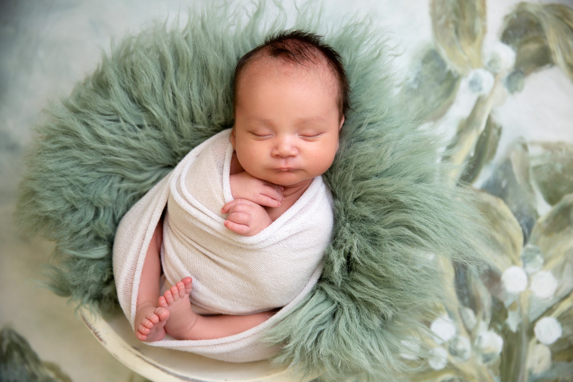 Newborn baby photographed wrapped in soft linen on green fluffy hair