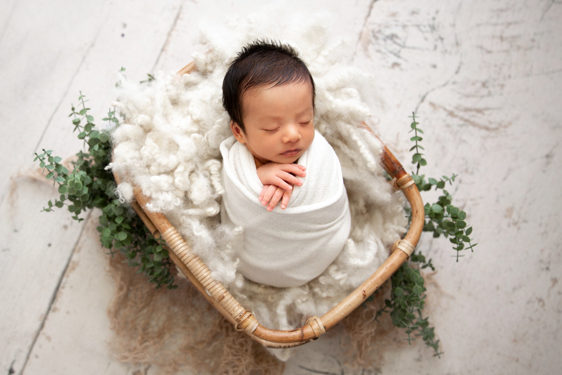 Tiny baby with brown hair wrapped up cozy sitting in a basket with cotton