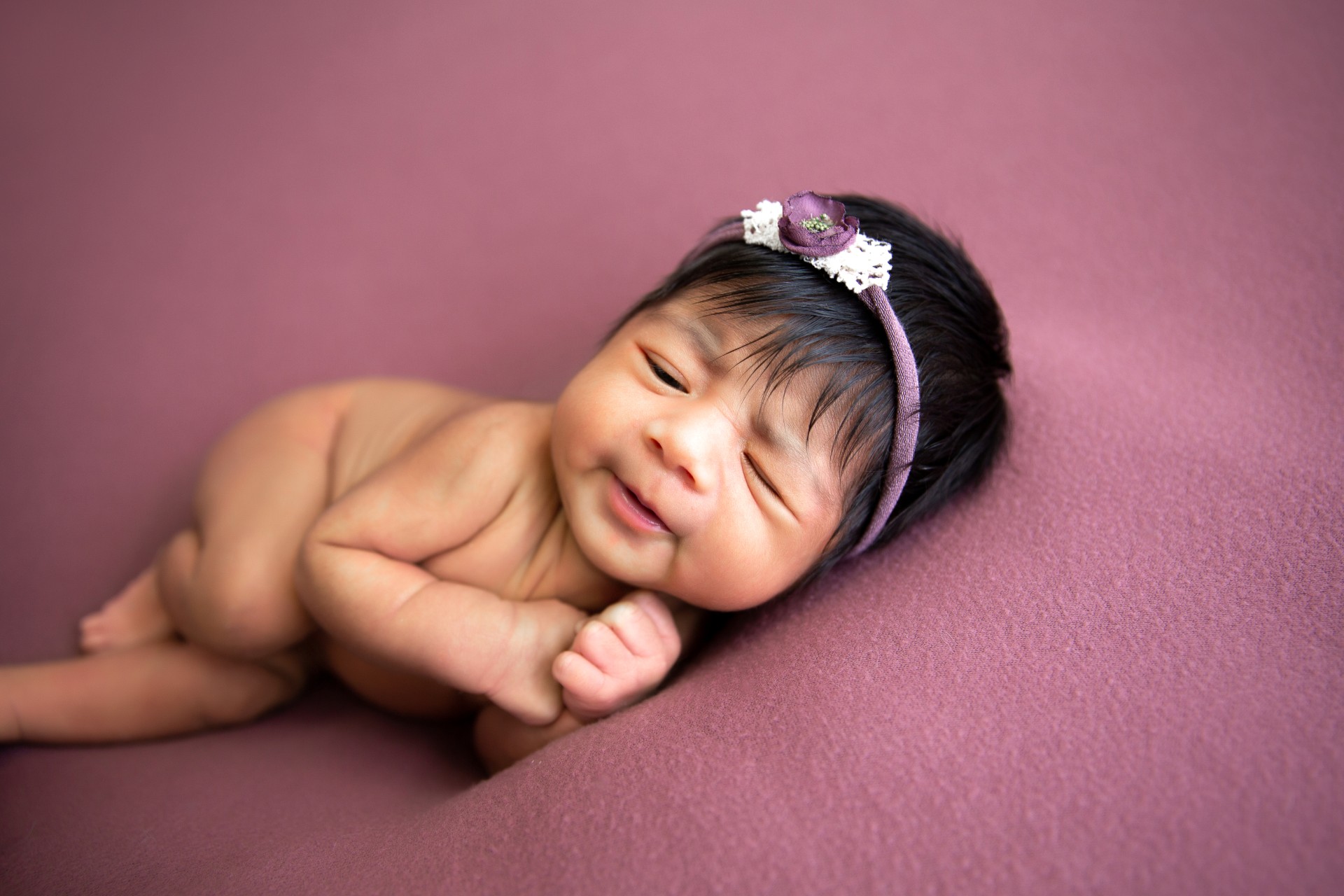 Newborn baby sleeping on a purple backdrop with a purple headband